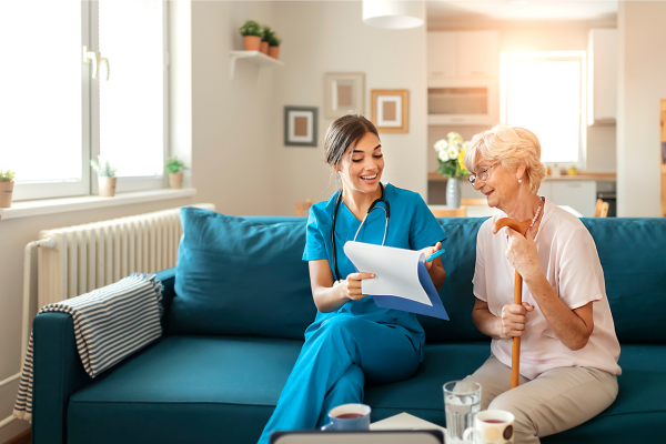 A nurse and an elderly patient sitting on a couch going over paperwork